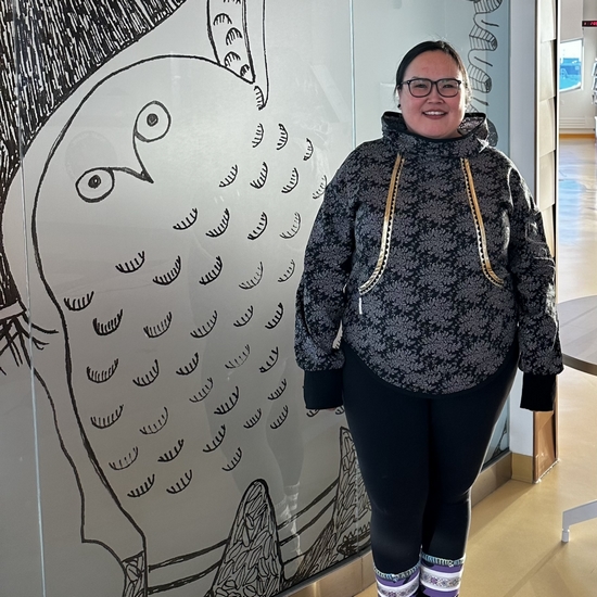 Kamele standing in front of artwork at the Canadian High Arctic Research Station, wearing a Kalikuk and embroidered kitikmeot style kamiit.